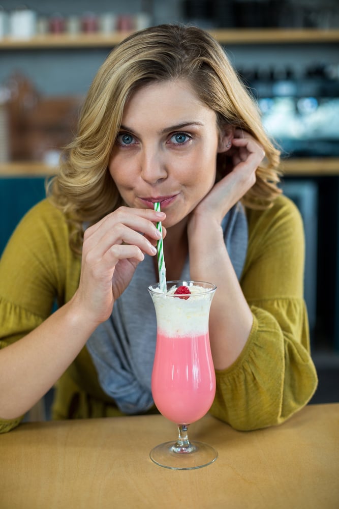 Portrait of woman drinking milkshake with a straw in cafe