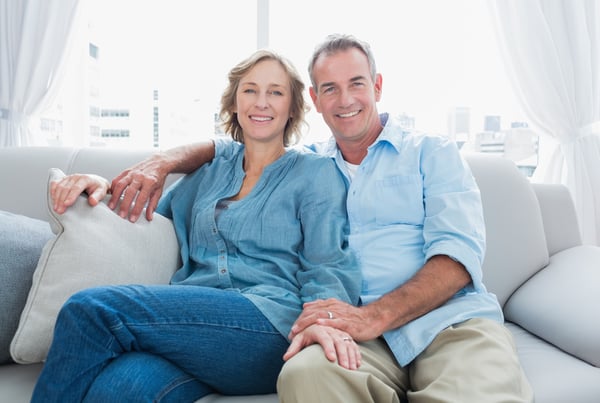 Middle aged couple relaxing on the couch smiling at camera at home in the living room